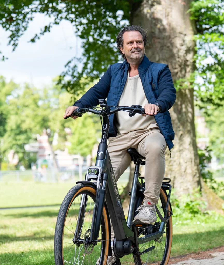 Impressie van merkfotografie voor LeaseGemak, waarop een casual geklede man op zijn fiets zit met zijn voet aan de grond, in een groen park.