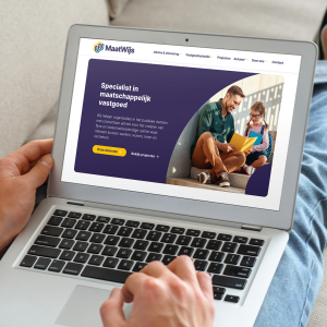 Man ligt op bank met laptop op schoot. Van over de schouder zie je het beeldscherm met de hero van de website van MaatWijs in beeld